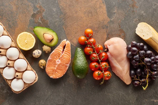 Vista superior de pescado crudo y aves de corral cerca de verduras, frutas, huevos y baguette en la superficie de mármol con espacio para copiar - foto de stock