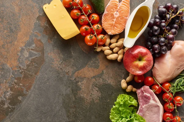 Vista superior de pescado crudo, carne y aves de corral cerca de verduras, frutas, queso, cacahuetes y aceite de oliva en la superficie de mármol con espacio para copiar - foto de stock