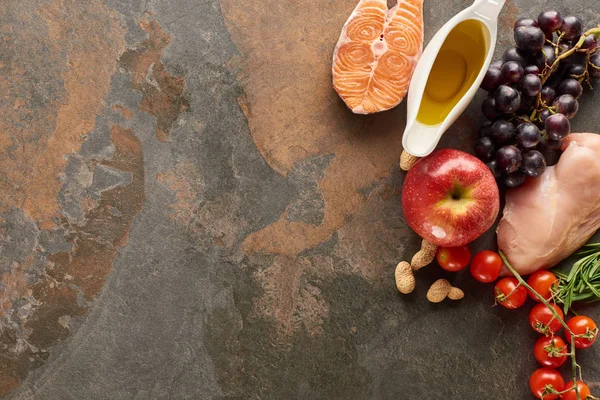 Top view of raw fish and poultry near vegetables, fruits, peanuts and olive oil on marble surface with copy space — Stock Photo