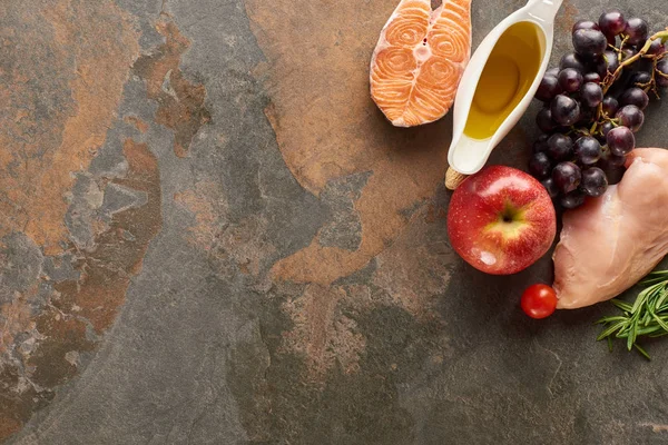 Vista superior de pescado crudo y aves de corral cerca de verduras, frutas, ramitas de hierbas y aceite de oliva en la superficie de mármol con espacio para copiar - foto de stock