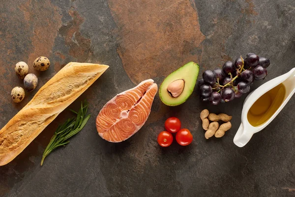 Ansicht von rohem Fisch in der Nähe von Gemüse, Obst, Eiern, Erdnüssen, Baguette, Kräuterzweigen und Olivenöl auf Marmoroberfläche mit Kopierfläche — Stockfoto