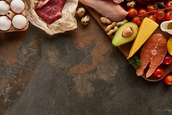 Ansicht des Holzschneidebretts mit rohem Fisch, Fleisch, Geflügel, Käse, Eiern, Gemüse und Erdnüssen auf dunkelbrauner Marmoroberfläche mit Kopierraum — Stockfoto