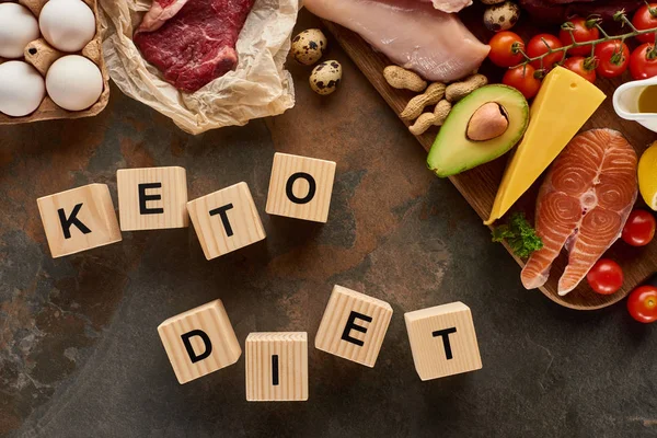 Top view of raw meat and fish near eggs, cheese, tomatoes, avocado and peanuts on marble surface with wooden cubes keto diet inscription — Stock Photo