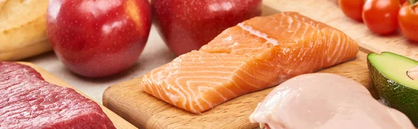 Foto panorámica de salmón crudo cerca de carne, aves y verduras en tablas de cortar de madera - foto de stock