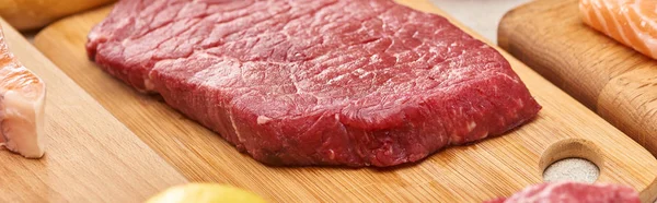 Tiro panorâmico de bife de carne crua na placa de corte de madeira — Fotografia de Stock