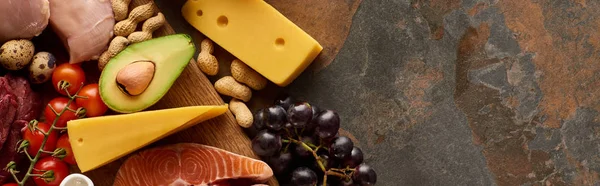 Panoramaaufnahme von frischem Gemüse und Obst mit rohem Fisch und Geflügel auf einem hölzernen Schneidebrett in der Nähe von Käse und Erdnüssen auf Marmoroberfläche — Stockfoto