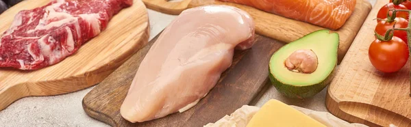 Panoramic shot of wooden cutting boards with raw meat and poultry fillet near avocado half and tomatoes — Stock Photo