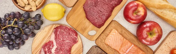 Panoramic shot of raw meat, fish and poultry on wooden cutting boards near fruits, lemon and peanuts — Stock Photo