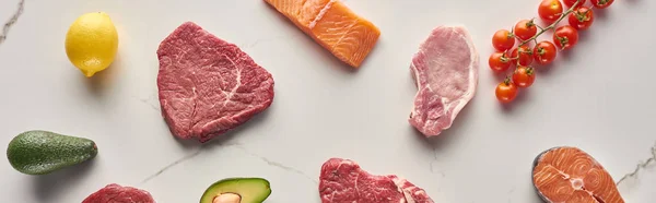 Foto panorámica de carne cruda y pescado cerca de aguacates, tomates y limón en la superficie de mármol - foto de stock