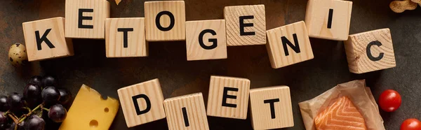 Panoramic shot of wooden cubes ketogenic inscription near cheese, grape, raw salmon, quail eggs and cherry tomatoes — Stock Photo