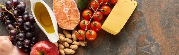 Panoramaaufnahme von rohem Lachssteak in der Nähe von Trauben, Tomaten, Erdnüssen, Äpfeln, Olivenöl und Käse auf Marmoroberfläche — Stockfoto