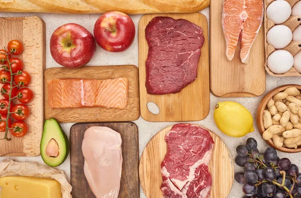 Vue de dessus de viande, volaille, poisson, œufs, fruits, légumes, fromage et baguette sur des planches à découper en bois — Photo de stock