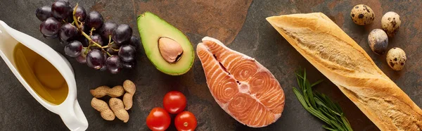 Панорамний знімок сирого лосося біля овочів, винограду, перепелиних яєць, арахісу, багетів та оливкової олії на мармуровій поверхні — стокове фото