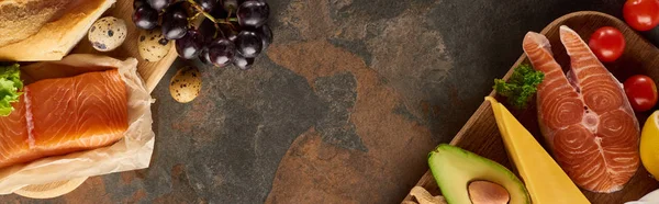 Panoramique des planches à découper en bois avec des parties de saumon cru, oeufs de caille, baguette, tomates, avocat, raisin, fromage sur la surface de marbre avec espace de copie — Photo de stock