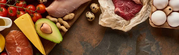 Foto panorámica de tabla de cortar de madera con pescado crudo y aves de corral cerca de verduras, queso, carne, huevos y cacahuetes en la superficie de mármol - foto de stock