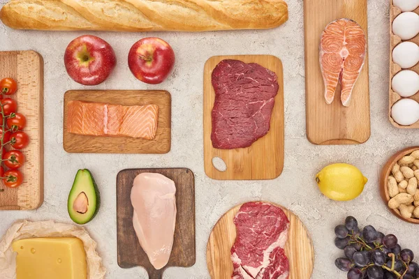 Vue de dessus de viande, volaille, poisson, œufs, fruits, légumes, fromage et baguette sur des planches à découper en bois à la surface du marbre — Photo de stock