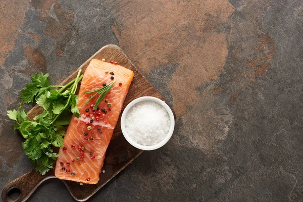 Vista superior del salmón fresco crudo con granos de pimienta, perejil y sal en la tabla de cortar de madera - foto de stock