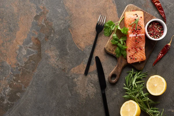 Top view of raw fresh salmon with greenery and lemon on wooden cutting board near cutlery — Stock Photo