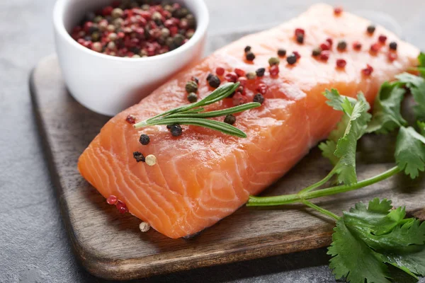 Raw salmon with peppercorns, parsley and rosemary on wooden cutting board — Stock Photo