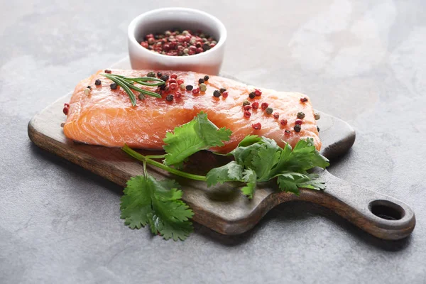 Salmón fresco crudo con granos de pimienta, perejil y romero sobre tabla de cortar de madera - foto de stock