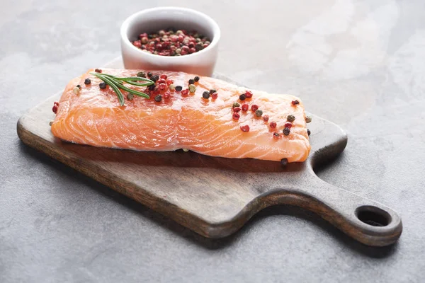 Salmón fresco crudo con granos de pimienta y romero sobre tabla de cortar de madera - foto de stock