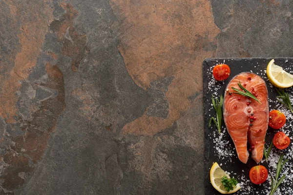 Вид на сырой лосось с приправами и помидорами на каменной доске — стоковое фото