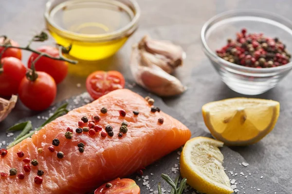 Selective focus of raw salmon with seasoning, lemon and tomatoes on stone board — Stock Photo