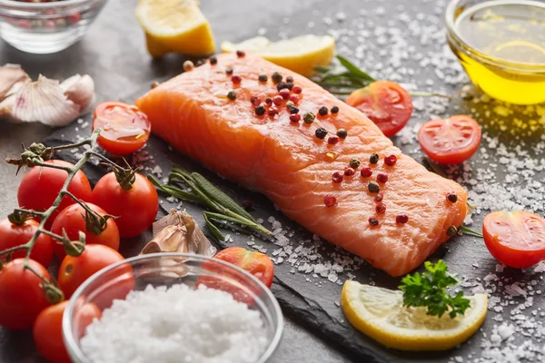 Raw salmon with seasoning and tomatoes on stone board with salt — Stock Photo
