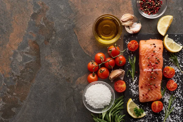 Top view of raw salmon with seasoning, oil, garlic and tomatoes on stone surface — Stock Photo