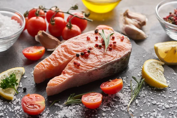 Raw salmon steak with seasoning and tomatoes on stone board — Stock Photo