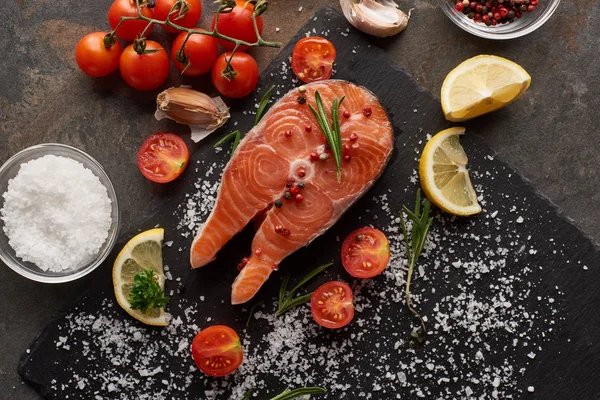 Top view of raw salmon with salt, lemon and tomatoes on stone board — Stock Photo