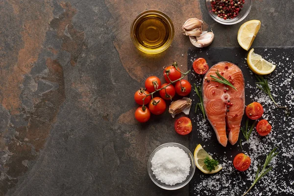 Top view of raw salmon with salt, rosemary and tomatoes on stone board — Stock Photo