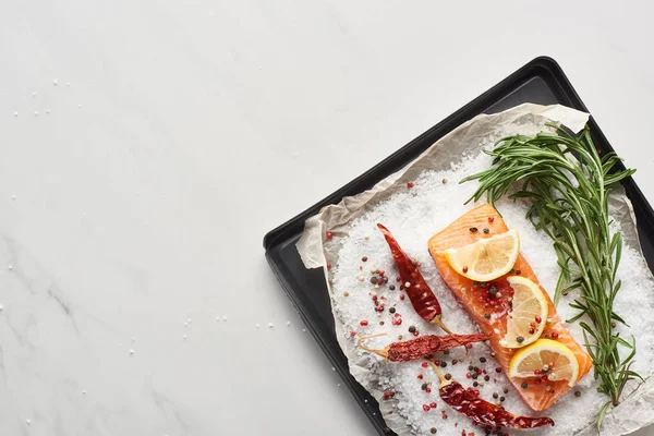 Vista superior de filete de salmón crudo con limón, romero y chiles en bandeja de horno con sal - foto de stock