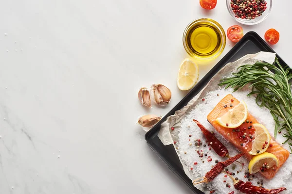 Top view of raw salmon steak with lemon, rosemary and chili peppers on oven tray with salt near garlic and oil — Stock Photo