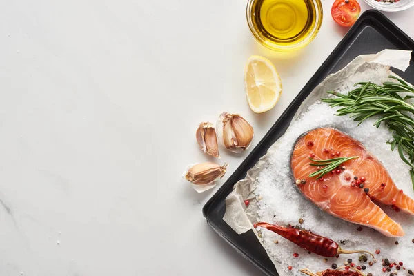 Top view of uncooked salmon steak with lemon, rosemary and chili peppers on oven tray with salt — Stock Photo