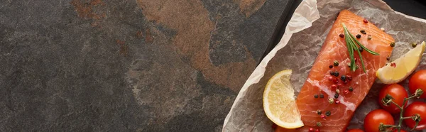 Panoramic shot of raw salmon steak with tomatoes, rosemary, lemon and pepper on bakery paper on oven tray — Stock Photo