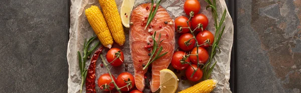 Plano panorámico de filete de salmón crudo con tomates, maíz, romero, limón sobre papel de panadería en bandeja de horno - foto de stock