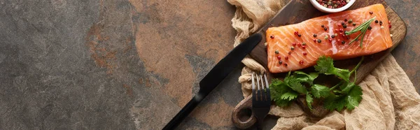 Vista superior de salmón fresco crudo con granos de pimienta, perejil sobre tabla de cortar de madera sobre tela rústica cerca de cuchillo y tenedor, plano panorámico - foto de stock