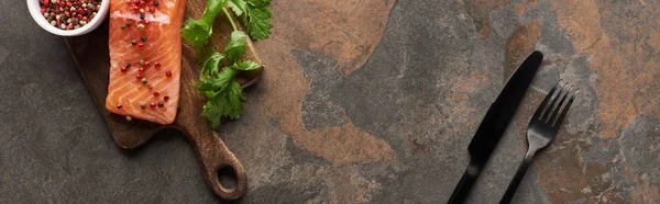 Vue du dessus du steak de saumon cru aux grains de poivre, persil sur planche à découper en bois près des couverts, vue panoramique — Photo de stock