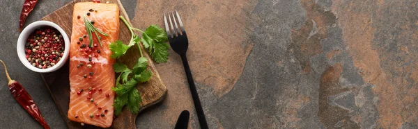 Vista dall'alto di salmone fresco crudo con grani di pepe, prezzemolo su tagliere di legno vicino a posate e peperoncini, colpo panoramico — Foto stock