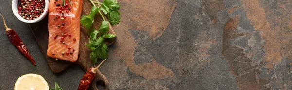 Top view of raw fresh salmon with peppercorns, parsley on wooden cutting board near lemon and chili peppers, panoramic shot — Stock Photo