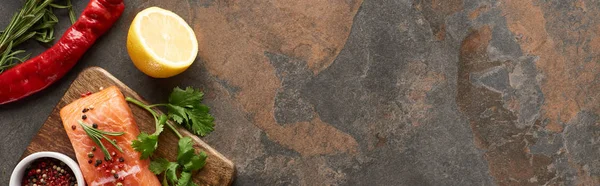 Top view of raw salmon with peppercorns, parsley on wooden cutting board near lemon and chili pepper, panoramic shot — Stock Photo