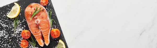 Top view of raw salmon with seasoning and tomatoes on stone board on marble table, panoramic shot — Stock Photo