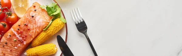 Vista dall'alto di bistecca di salmone crudo con mais, limone e pomodori sul piatto vicino posate sul tavolo di marmo, colpo panoramico — Foto stock