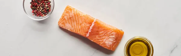 Top view of raw salmon steak near oil and peppercorns in bowls on marble table, panoramic shot — Stock Photo