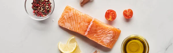 Vista dall'alto di bistecca di salmone crudo vicino al limone, pomodori, aglio, olio e grani di pepe in ciotole sul tavolo di marmo, colpo panoramico — Foto stock