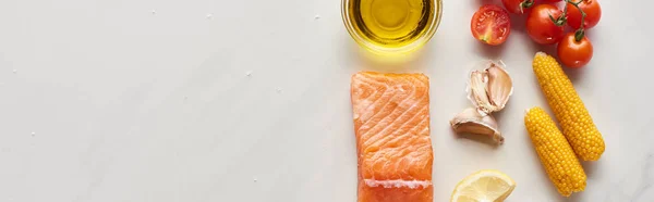 Top view of raw salmon steak near lemon, corn, tomatoes, garlic, oil and peppercorns in bowls on marble table, panoramic shot — Stock Photo