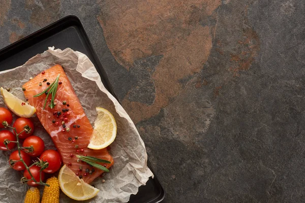 Vue du dessus du steak de saumon non cuit avec tomates, maïs, citron, romarin et poivre sur le plateau du four — Photo de stock