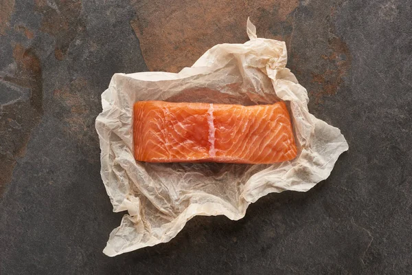 Vue du dessus du steak de saumon non cuit sur papier de boulangerie sur table en pierre — Photo de stock