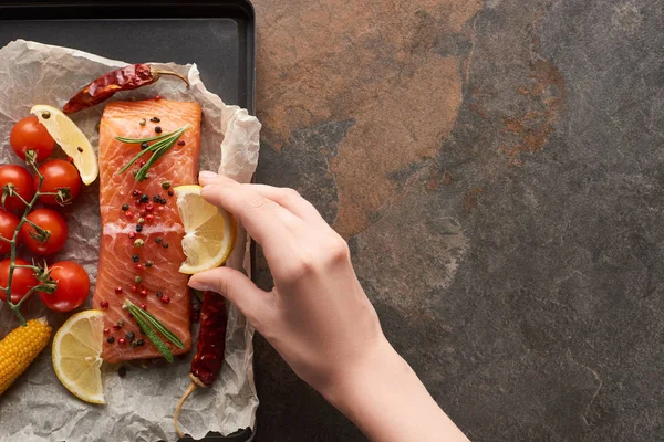 Cropped view of woman squeezing lemon juice on uncooked salmon steak with vegetables on oven tray — Stock Photo